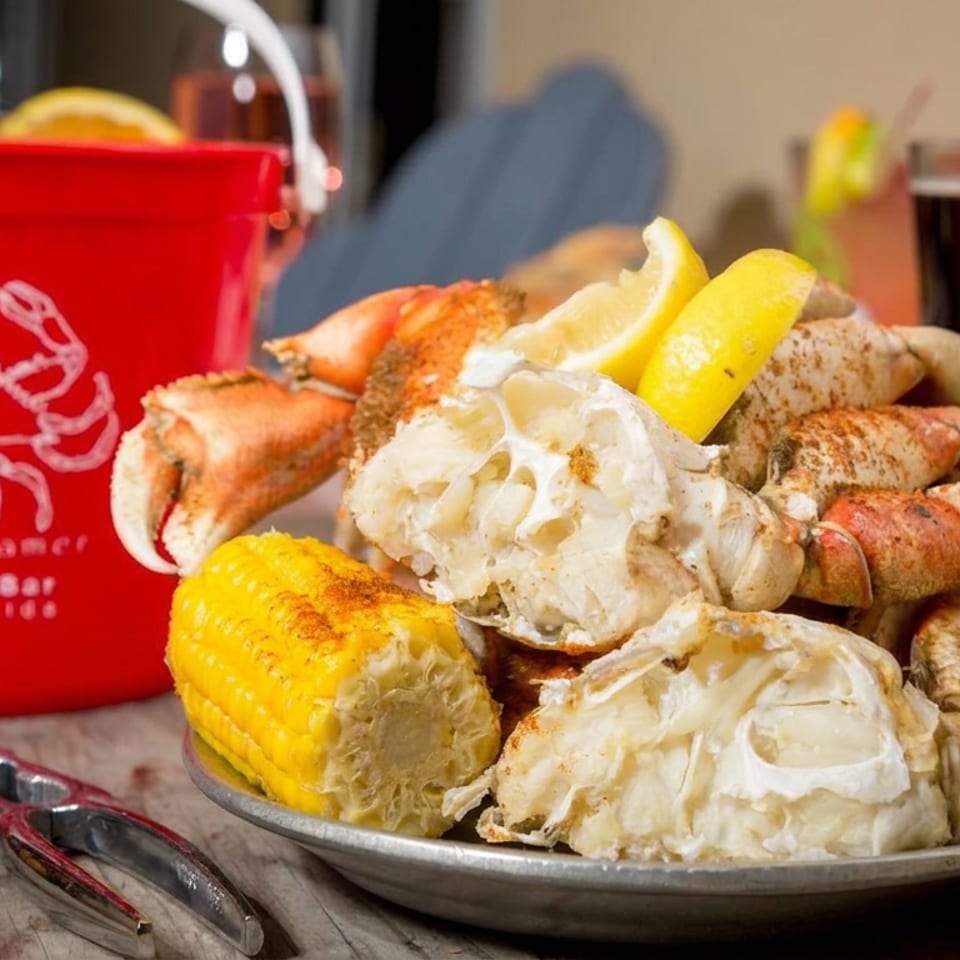 Steamed seafood platter with crab legs, shrimp, corn, and lemon beside a red Seafood Steamers bucket.
