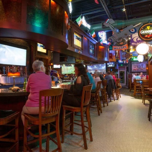 Lively Irish-style pub interior with patrons seated at the bar, televisions, sports memorabilia, and Guinness signage.