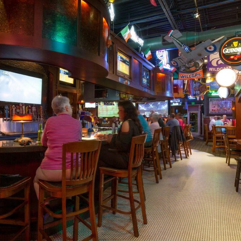 Lively Irish-style pub interior with patrons seated at the bar, televisions, sports memorabilia, and Guinness signage.