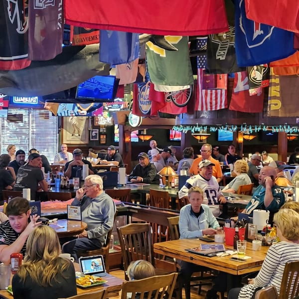 Busy sports bar filled with diners, hanging team jerseys, flags, and multiple televisions broadcasting games.