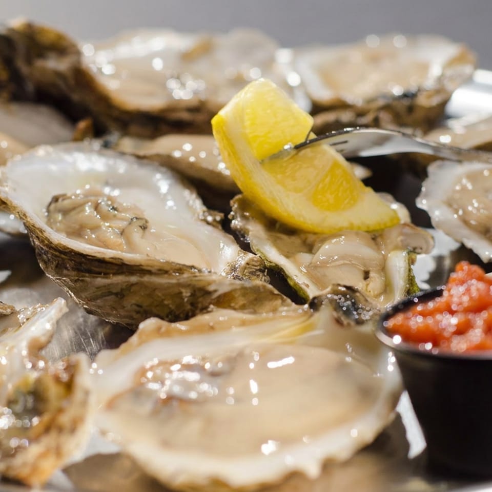 Platter of freshly shucked oysters with lemon wedges, cocktail sauce, and a fork.