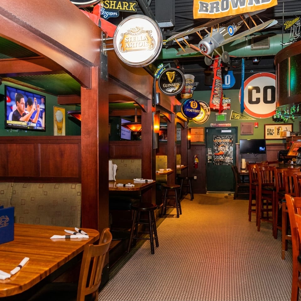 Sports bar interior with wooden tables, televisions, beer signs, aviation decor, and a polished bar counter.