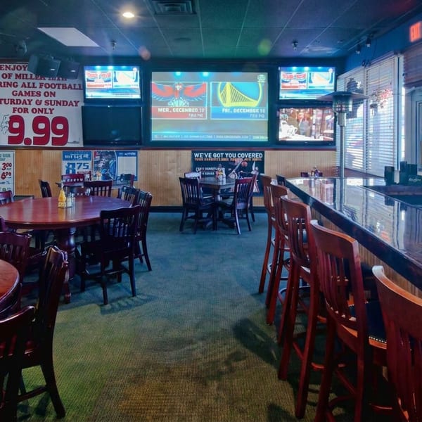 Empty sports bar dining area with wooden tables, bar seating, multiple televisions, and football promotions on the walls.