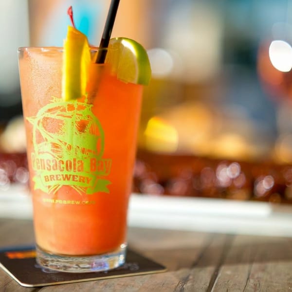 Bright orange cocktail garnished with citrus slices in a Gasparilla Bay Brewery glass, resting on a wooden restaurant table.