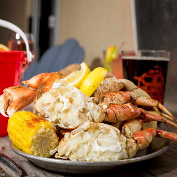 A platter of steamed crab legs and corn on the cob with lemon wedges and drinks.