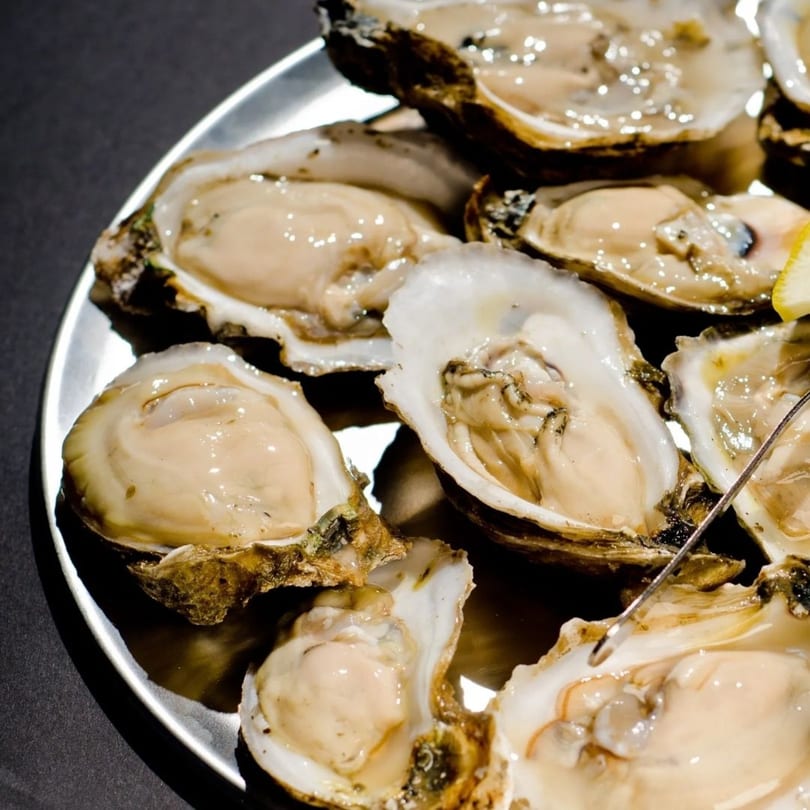 A close-up of fresh, shucked oysters on a silver platter, ready to be enjoyed.