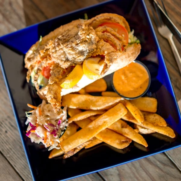 Fried soft-shell crab po'boy with fries, coleslaw, and dipping sauce on a blue plate.