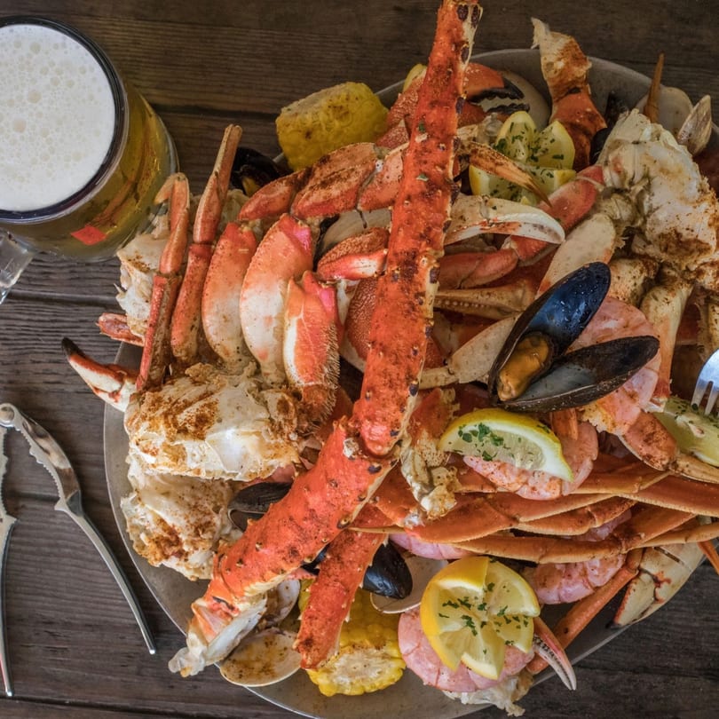 O'Quigley's seafood boil with crab legs, mussels, shrimp, corn, and lemon, alongside a beer.
