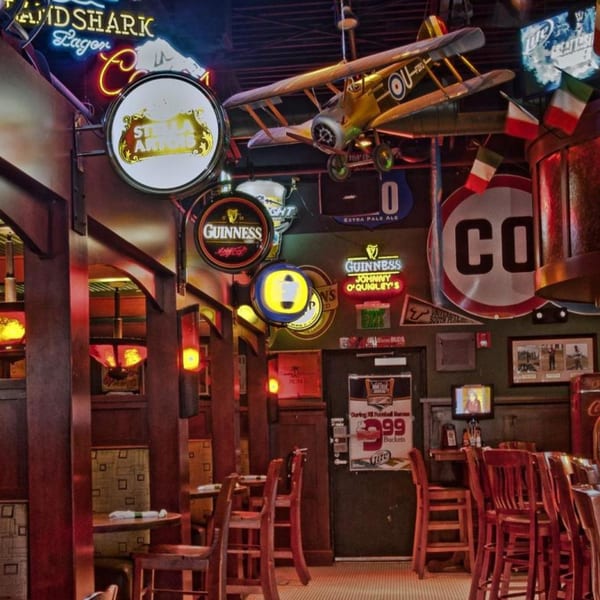 A lively bar interior with neon signs, a model airplane, and wooden tables and chairs.