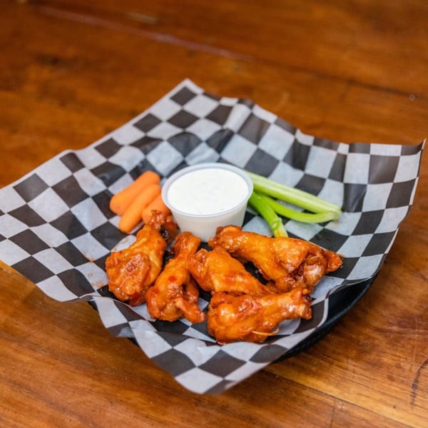 Buffalo wings with ranch, carrots, and celery on checkered paper in a basket.