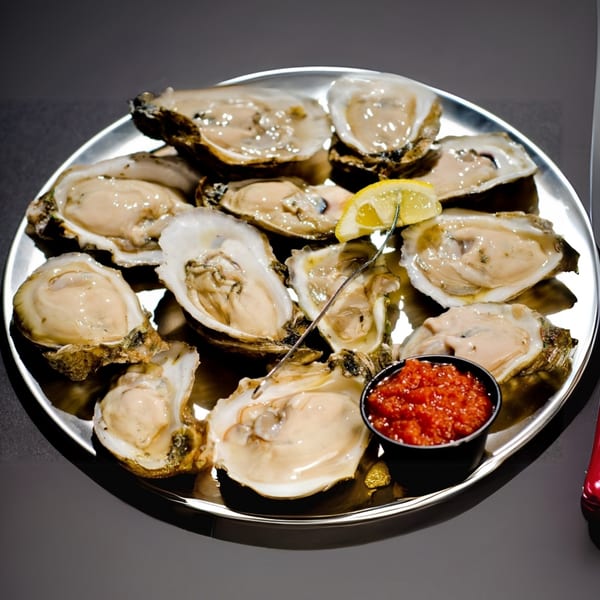 A dozen fresh oysters on a silver platter with lemon and red cocktail sauce.