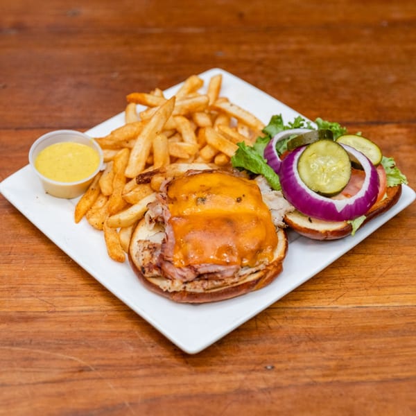 A cheeseburger with fries and a side of mustard on a white plate on a wooden table.